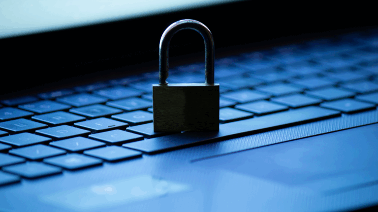 A padlock stands on top of a computer with the computer screen glow in the background.