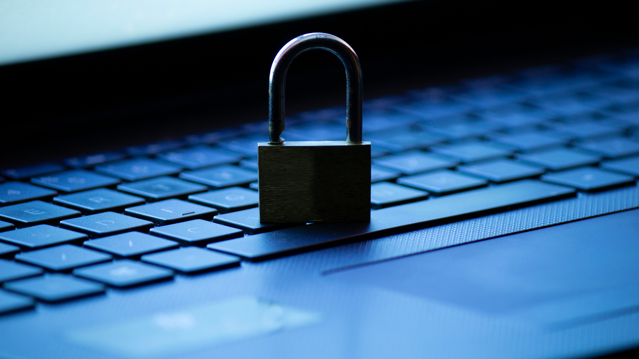 A padlock stands on top of a computer with the computer screen glow in the background.