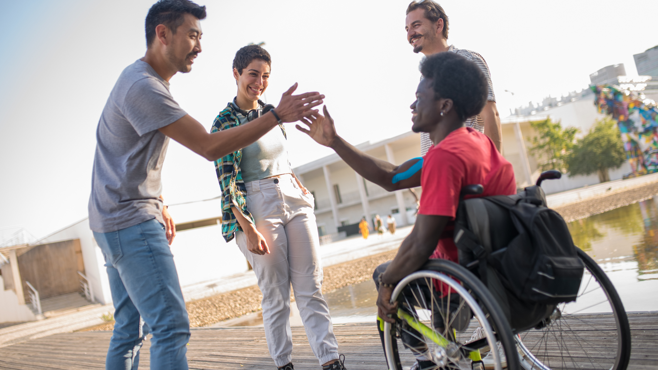Group of four people high five outside and laugh together. One individual is in a wheelchair.